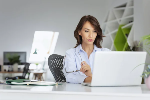 拍了一个漂亮的中年妇女坐在办公桌前 使用笔记本电脑 漂亮的女人穿着休闲装 总部办公室 — 图库照片