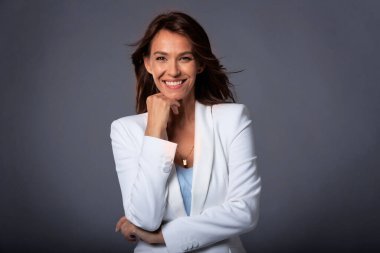 Çekici, orta yaşlı, dişlek gülümseyen, ceketli, karanlık arka planda oturan bir kadının yakın çekimi. Uzayı kopyala Stüdyo çekimi.