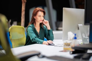 Ofiste masa başında otururken bilgisayar kullanan orta yaşlı bir iş kadını. Finansal raporlar üzerinde çalışan profesyonel bir kadın..