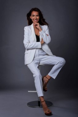 Çekici, orta yaşlı, dişlek, takım elbiseli, koyu tenli arka planda oturan bir kadın. Uzayı kopyala Stüdyo çekimi.