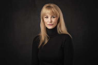 Güzel, gülümseyen bir kadın soyutlanmış, karanlık arka planda duruyor. Balıkçı yaka kazak giyen sarışın kadın. Boşluğu kopyala. 