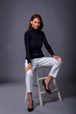 Çekici, orta yaşlı, dişlek, siyah bir süveter giyen, izole, koyu bir arka planda oturan bir kadın. Uzayı kopyala Stüdyo çekimi.