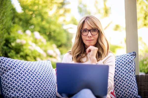 自宅の裏庭に座って仕事のために彼女のラップトップを使用して魅力的な中年の女性 内務省 — ストック写真