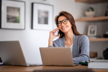 Happy woman using mobile phone and laptops for work. Confident business woman working from home. Home office. 