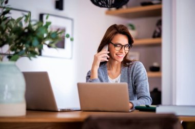 Happy woman using mobile phone and laptops for work. Confident business woman working from home. Home office. 