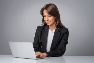 İş için dizüstü bilgisayar kullanan çekici bir iş kadınının stüdyo fotoğrafı. Gri arka planda oturan gülümseyen kadın. Boşluğu kopyala.