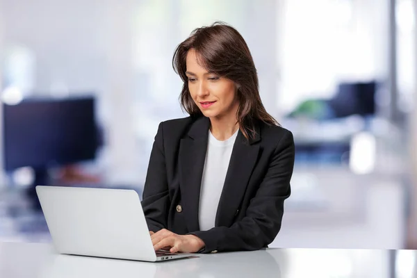 迷人的女商人穿着西装 工作时使用笔记本电脑 微笑着坐在办公室里工作的女性 — 图库照片