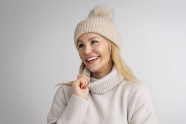 İzole edilmiş beyaz arka planda duran güzel, gülümseyen kadın. Sarı saçlı, örgü şapka ve balıkçı yaka kazak giyen bir kadın. Boşluğu kopyala. 