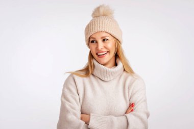 İzole edilmiş beyaz arka planda duran güzel, gülümseyen kadın. Sarı saçlı, örgü şapka ve balıkçı yaka kazak giyen bir kadın. Boşluğu kopyala. 