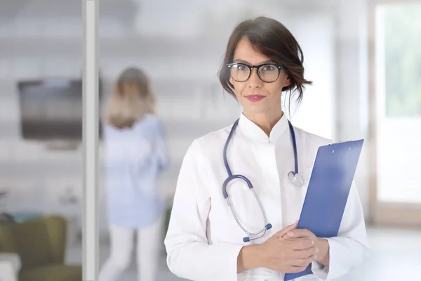 女医生穿着实验室外套和听诊器 手握剪贴板站在医院走廊 — 图库照片