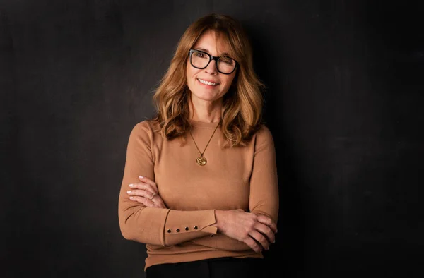 stock image Close-up of an attractive middle aged woman smiling and looking at camera. Blond haired female wearing casual clothes and standing against isolated dark background. Copy space. Studio shot. 