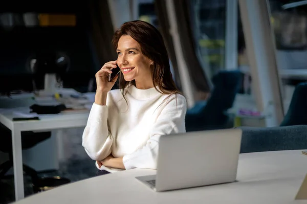 オフィスに座っている間 ラップトップを使用して電話を持っている中年のビジネス女性 セーターを着た魅力的なビジネス女性 — ストック写真