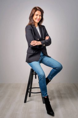 Ceket ve kot pantolon giyen çekici bir kadının stüdyo portresi izole edilmiş arka planda otururken. Tam yol ileri. Boşluğu kopyala. 