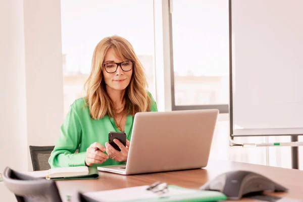 Portrait Confident Smiling Businesswoman Sitting Her Laptop Using Mobile Phone — стоковое фото