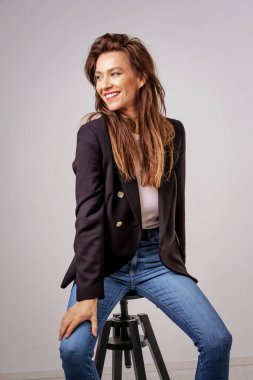 Gri arka planda oturan güzel, gülümseyen bir kadının stüdyo fotoğrafı.. 