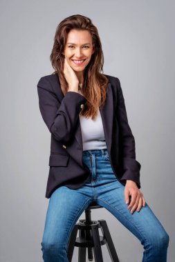 Gri arka planda oturan güzel, gülümseyen bir kadının stüdyo fotoğrafı.. 