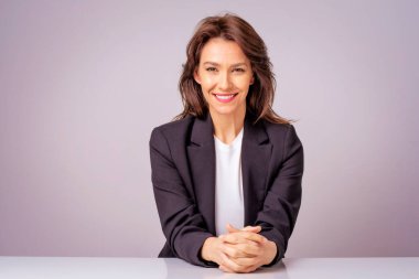 Gri arka planda otururken siyah ceket giyen çekici bir iş kadınının portresi. Boşluğu kopyala. 