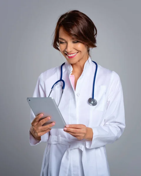 ライトグレーの背景を背景に立っている間 女性医師の肖像画は デジタルタブレット上で彼女の患者チャートを保持 — ストック写真