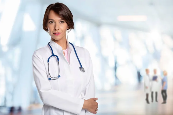 研究室のコートと聴診器を身に着けて病院の廊下に立つ笑顔の女性医師 — ストック写真