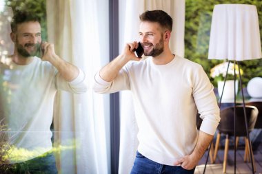 Pencerenin önünde duran ve telefon eden yakışıklı bir adamın portresi. Gündelik kıyafetler giyen kendinden emin bir erkek..