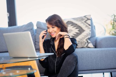 Çekici esmer saçlı, neşeli gülümseyen kadın. İş için cep telefonu ve laptop kullanan orta yaşlı bir kadın. Merkez Ofis.
