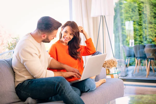 幸せなカップル一緒にソファの上でリラックス インターネットで閲覧しながらノートパソコンを使って朗らかな女とハンサムな男 指で画面に何かを見せる男 — ストック写真
