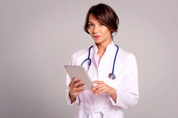 一位女医生站在浅灰背景下 将病历放在数码平板上的肖像 复制空间 — 图库照片