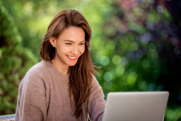 バルコニーに座ってノートパソコンを持つ笑顔の中年女性 美しい女性がブルネットの髪を持っているとカジュアルな服を着て — ストック写真