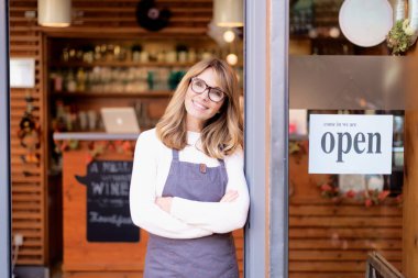 Gülümseyen kafe sahibi iş kadınının portre fotoğrafı. Kapıda kollarını kavuşturup misafirini bekliyor..
