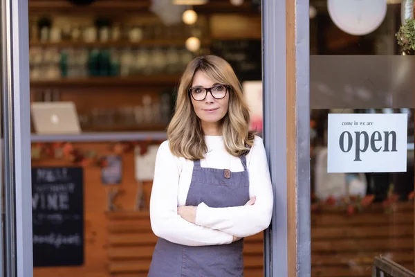 笑顔のカフェオーナーの肖像画ビジネス女性は折り畳まれた腕で戸口に立って 彼女のゲストを待っています — ストック写真