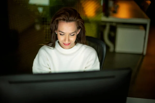 Zdjęcia Uśmiechniętej Bizneswoman Siedzącej Przy Stole Komputerem Biurze Późnym Wieczorem — Zdjęcie stockowe