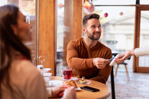 一对夫妇坐在咖啡店的餐桌旁 男人用卡片支付女服务员的特写镜头 网上支付 — 图库照片