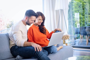 Mutlu çift evdeki kanepede dinleniyor. İnternette laptop ve browisng kullanan çekici orta yaşlı kadın ve yakışıklı erkek..