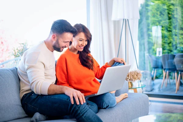 这对快乐的夫妇在家里的沙发上休息 有魅力的中年女性和英俊男性使用笔记本电脑在网上浏览或通过视频通话 — 图库照片