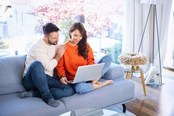 这对快乐的夫妇在家里的沙发上休息 有魅力的中年女性和英俊男性使用笔记本电脑在网上浏览或通过视频通话 — 图库照片