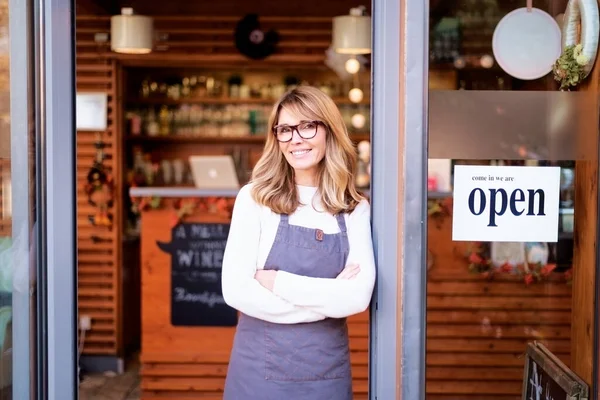 一位自信的女店主站在咖啡店门口的画像 布鲁内特留着漂亮的头发 看着相机 面带微笑 — 图库照片