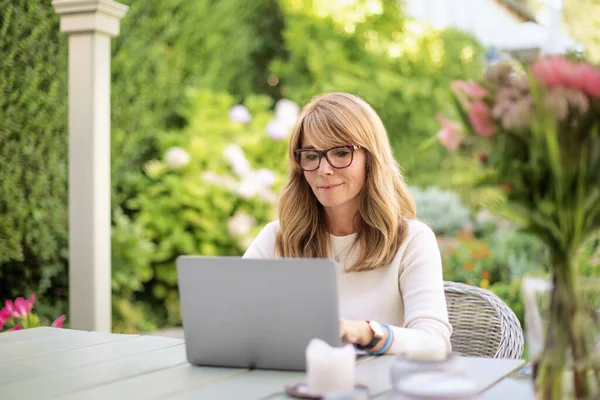 微笑的金发女人坐在家里的阳台上 用笔记本电脑工作 在互联网上打电话或浏览的女商人 — 图库照片