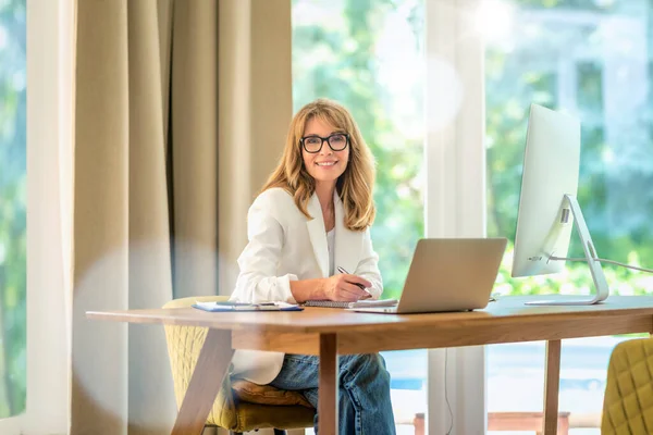 Χαρούμενη Χαμογελαστή Μεσήλικη Επιχειρηματίας Που Κάθεται Στο Γραφείο Και Χρησιμοποιεί — Φωτογραφία Αρχείου