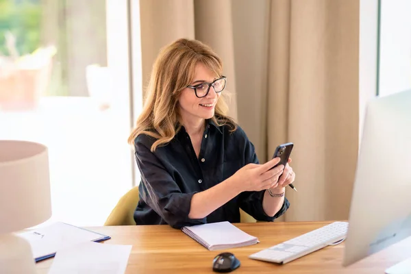 中年妇女坐在办公桌前 用手机射击 自信的女性 戴着眼镜 穿着休闲装 在家工作 总部办公室 — 图库照片
