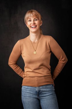 Güzel, gülümseyen bir kadın soyutlanmış, karanlık arka planda duruyor. Süveter giyen sarı saçlı kadın. Boşluğu kopyala. 