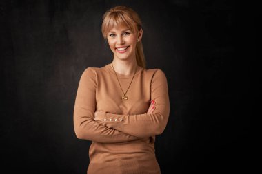 Güzel, gülümseyen bir kadın soyutlanmış, karanlık arka planda duruyor. Süveter giyen sarı saçlı kadın. Boşluğu kopyala. 