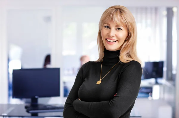 オフィスに立っている金髪の女性のクローズアップ カメラと陽気な笑顔を見ながらタートルネックセーターを着ている魅力的なビジネスマン コピースペース ロイヤリティフリーのストック写真