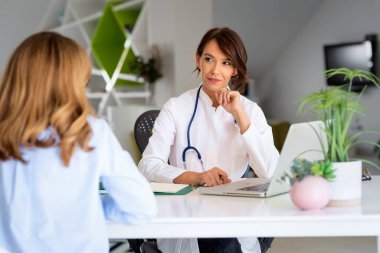 Ofiste çalışan ve semptomlarını açıklayıp danışmanlık yaparken hastayı dinleyen kadın doktor..