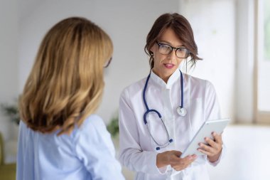 Female doctor standing on the corridor and using digital tablet while she is explaining her symptoms to the patient.