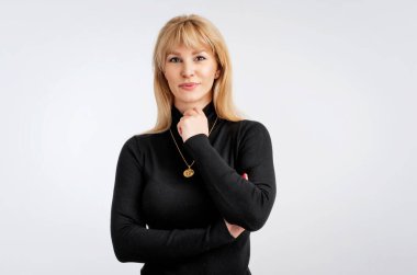 Siyah kazak giyen yakın plan sarışın kadın. Kollarını kavuşturmuş gülümseyen bir kadın. Gri arka plana karşı. Boşluğu kopyala.