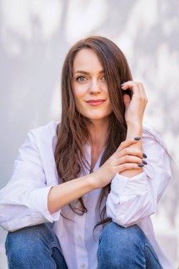 Gülümseyen güzel bir genç kadının portresi. Çekici genç bayan yeşil gözlü, uzun esmer saçlı ve dışarıda güneşin altında oturuyor. Boşluğu kopyala.