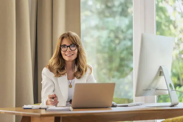 金发女商人坐在她的办公桌前 在她的笔记本电脑上工作或有视频通话 穿着眼罩和白衣的职业女性 — 图库照片