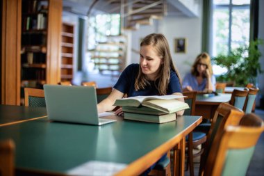 Üniversite kütüphanesinde oturan ve okuyan görme engelli genç bir kadın. Genç bir kadın kitap kullanıyor ve notlar alıyor..  