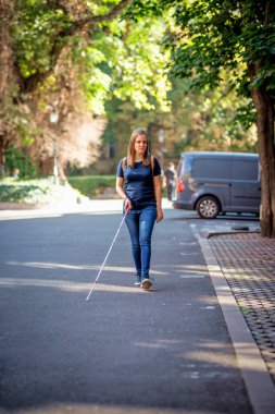 Sokakta yürüyen beyaz bastonlu kör kadın portresi. Sıradan kıyafetler giyen ve sopasıyla karşıya geçen görme engelli bir kadın. Tam boy çekim.