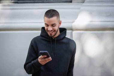 Şehirde sokakta dikilirken yakışıklı bir gencin cep telefonunu kullanırken çekilmiş bir fotoğrafı. Kapüşonlu ve kısa mesajlı kendinden emin bir adam..